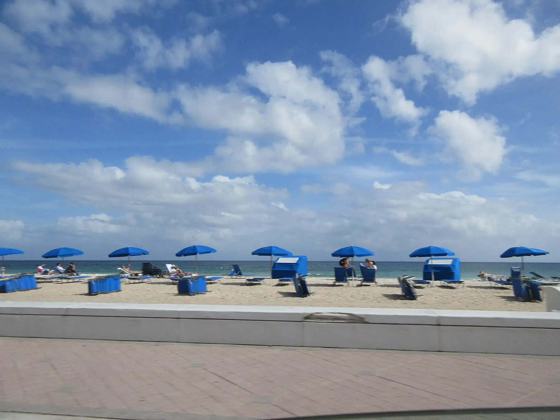 Blue beach umbrellas and cabanas on Fort Lauderdale Beach behind the wave wall